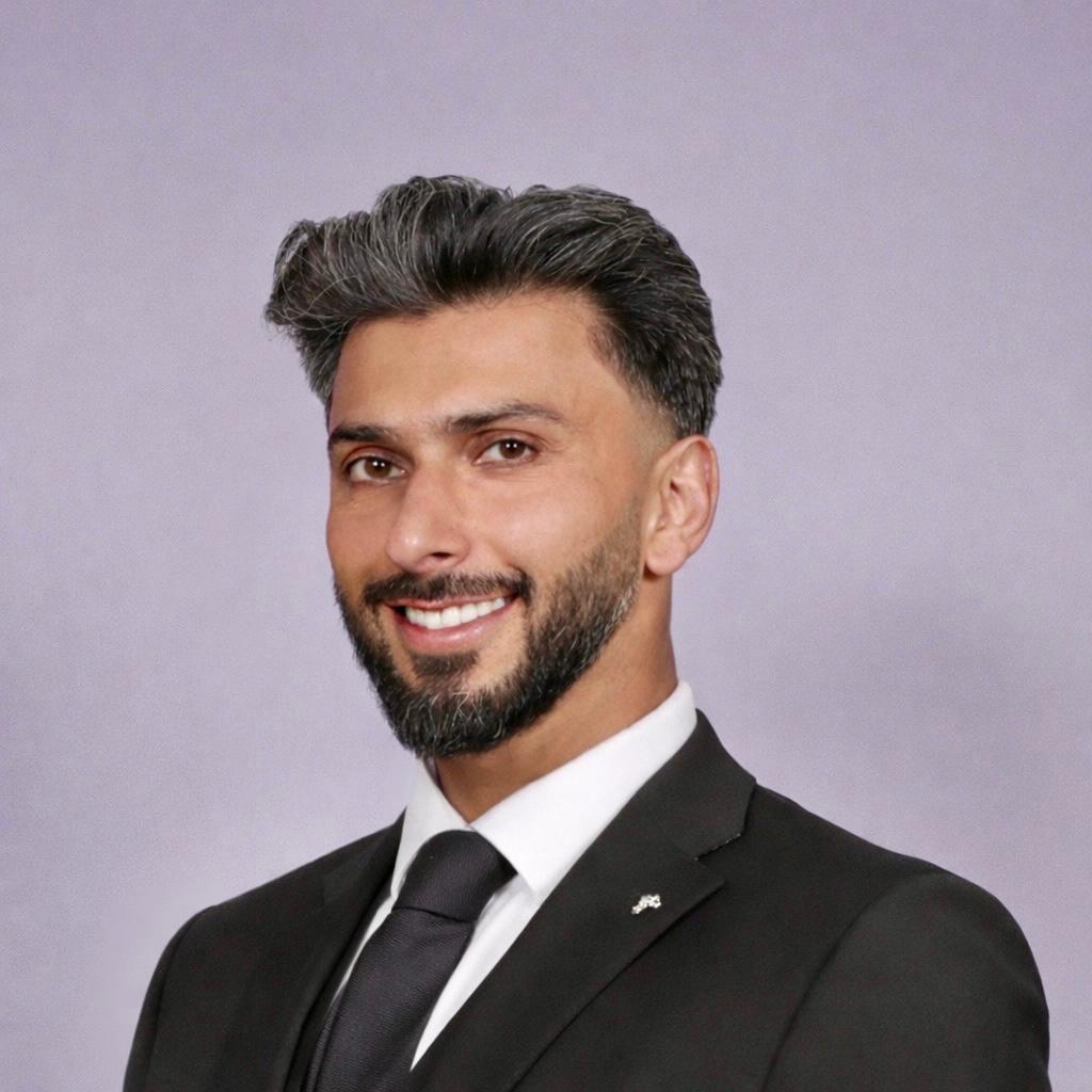 Bilal Ejaz, Advocacy AI team member, in a black suit with white shirt and dark tie, smiling against a plain light purple background, professional headshot style.