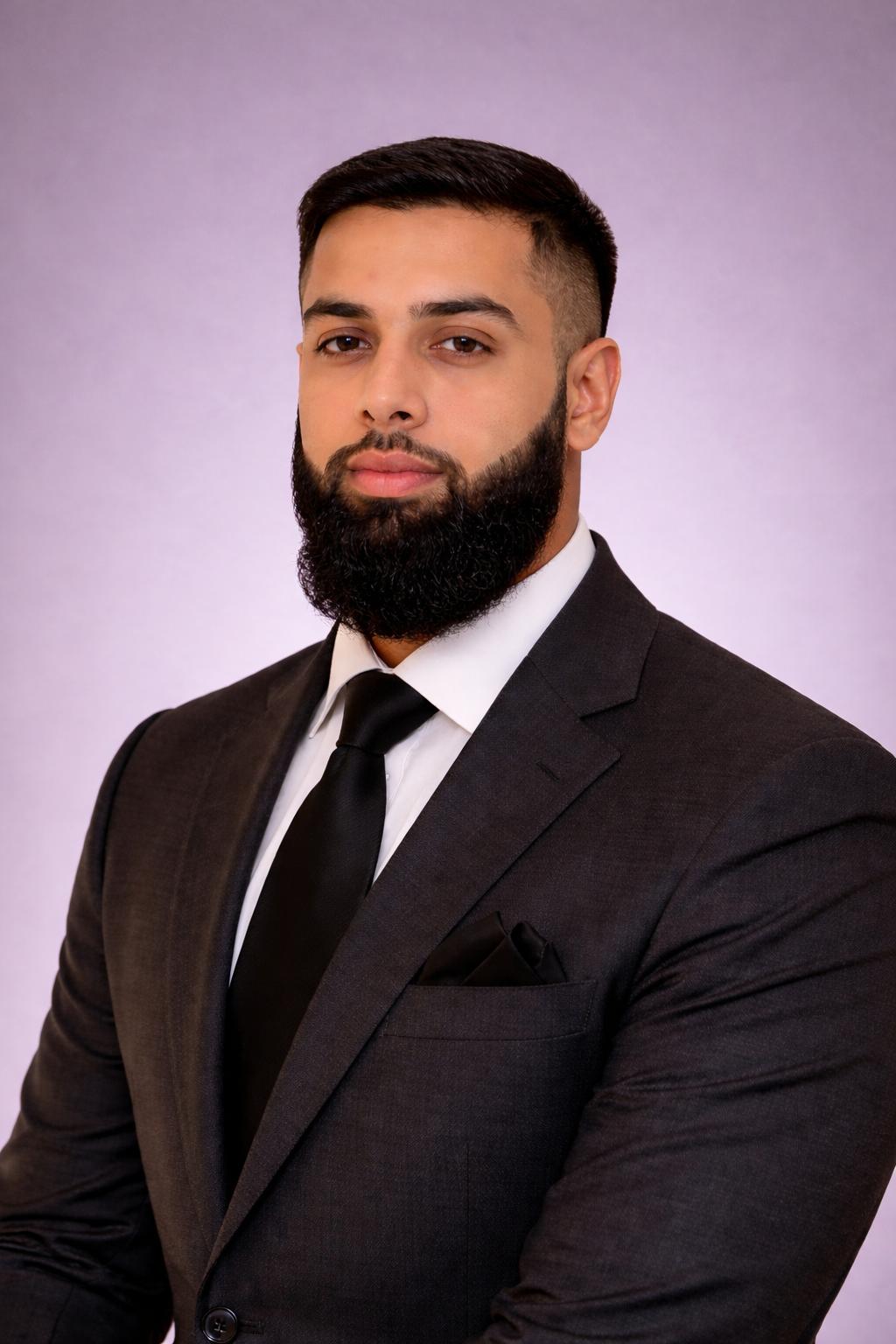 Rahat Shah, Advocacy AI team member, in a dark gray suit with white shirt and black tie against a light purple background