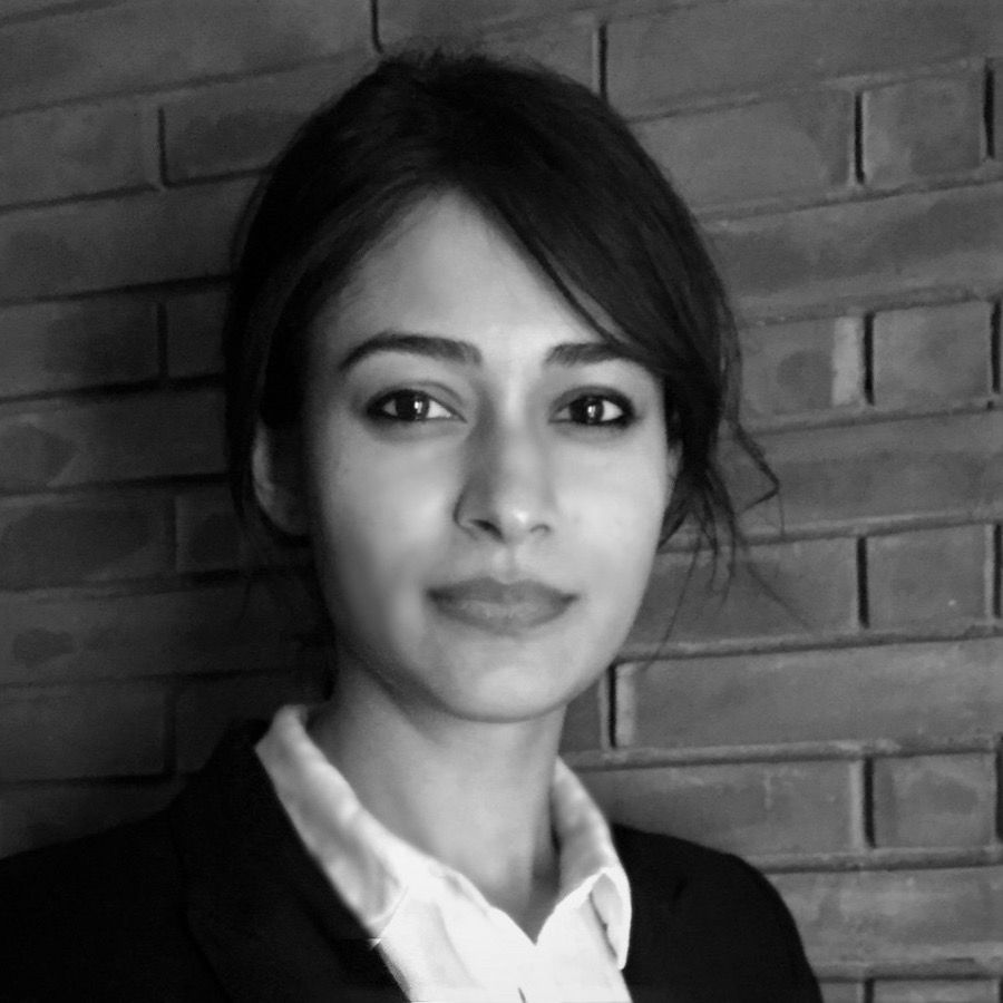 Shaffaf Shahid Latif, Advocacy AI team member, in a collared shirt and blazer with hair neatly tied back, grayscale portrait against a brick wall background, formal professional style.