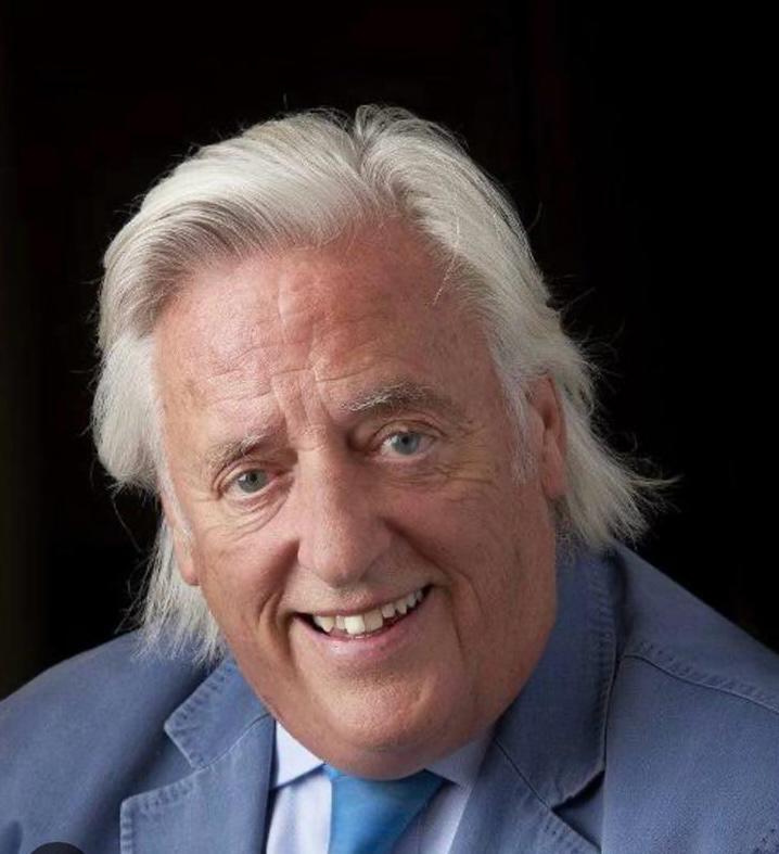 Michael Mansfield, Advocacy Advisory International team member, in light blue suit jacket, white shirt, and blue tie. Smiling with light‑coloured hair against dark background, professional portrait emphasising approachability and expertise.